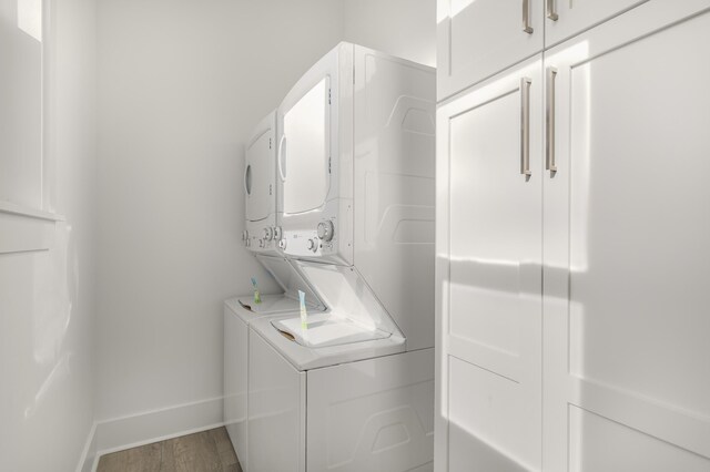 clothes washing area featuring hardwood / wood-style flooring, cabinets, and stacked washing maching and dryer