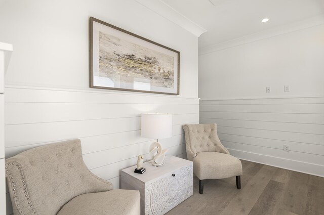 sitting room with hardwood / wood-style flooring, wooden walls, and crown molding