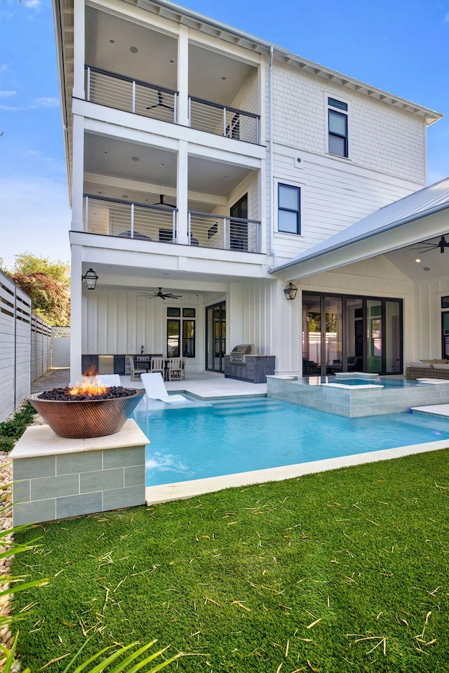 back of property featuring a fire pit, ceiling fan, a balcony, a lawn, and a fenced in pool