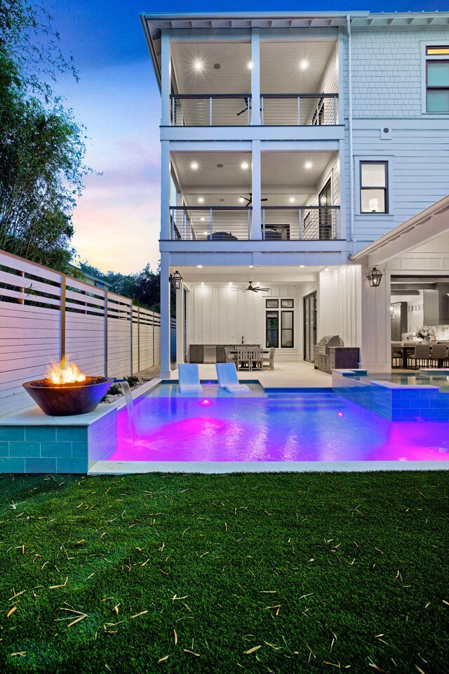 back house at dusk with a fire pit, a balcony, a yard, and pool water feature