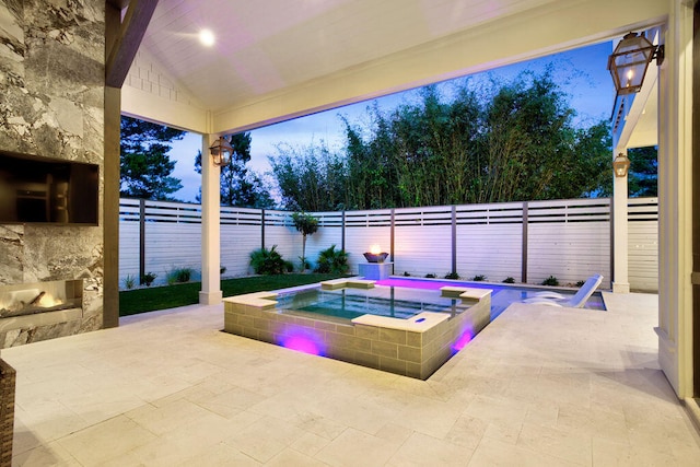 pool at dusk featuring a patio area and an in ground hot tub