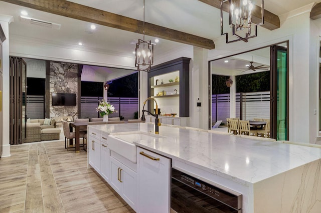 kitchen featuring light stone countertops, decorative light fixtures, a center island with sink, beverage cooler, and ceiling fan with notable chandelier