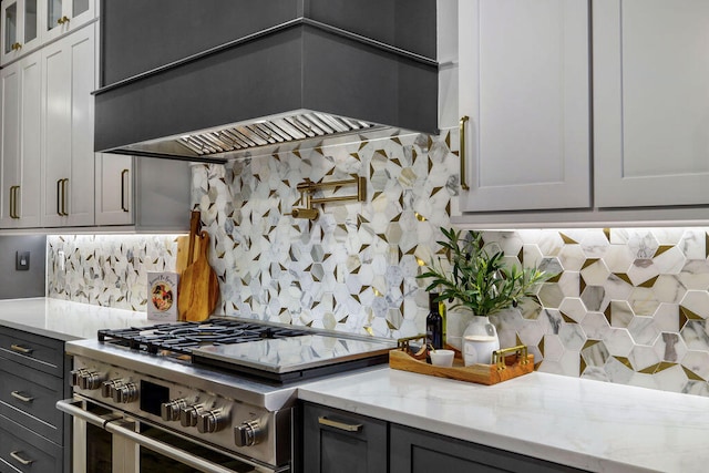 kitchen with premium range hood, high end stainless steel range oven, gray cabinets, backsplash, and light stone counters