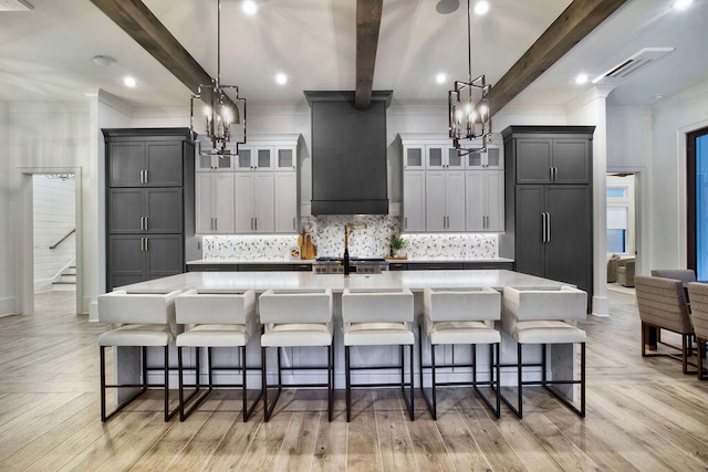 kitchen with hanging light fixtures, an island with sink, and premium range hood