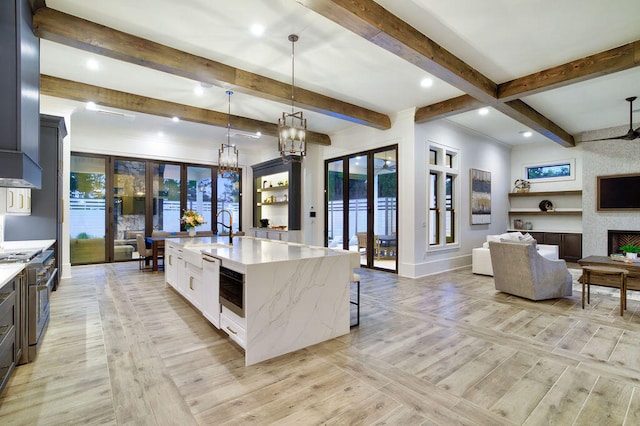 kitchen with a healthy amount of sunlight, a kitchen island with sink, decorative light fixtures, light stone countertops, and beam ceiling