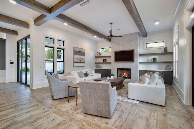 living room with beamed ceiling, ceiling fan, light hardwood / wood-style floors, and a large fireplace