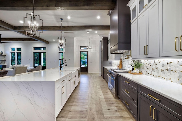 kitchen featuring double oven range, white cabinets, hanging light fixtures, beam ceiling, and premium range hood