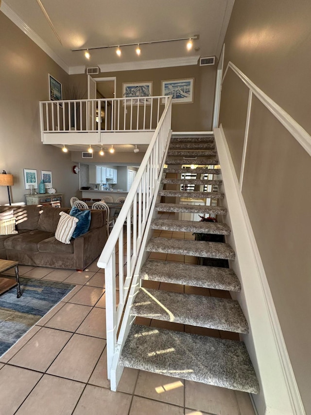 stairs featuring rail lighting, ornamental molding, and light tile floors