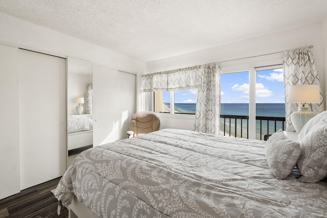 bedroom with multiple windows, a water view, access to exterior, and dark wood-type flooring