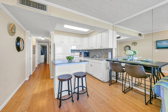 kitchen featuring white appliances, white cabinetry, light hardwood / wood-style flooring, and a breakfast bar area