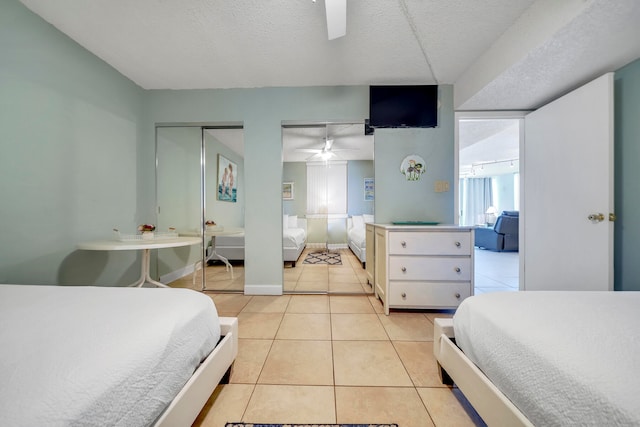 bedroom featuring a textured ceiling, ceiling fan, light tile floors, and two closets