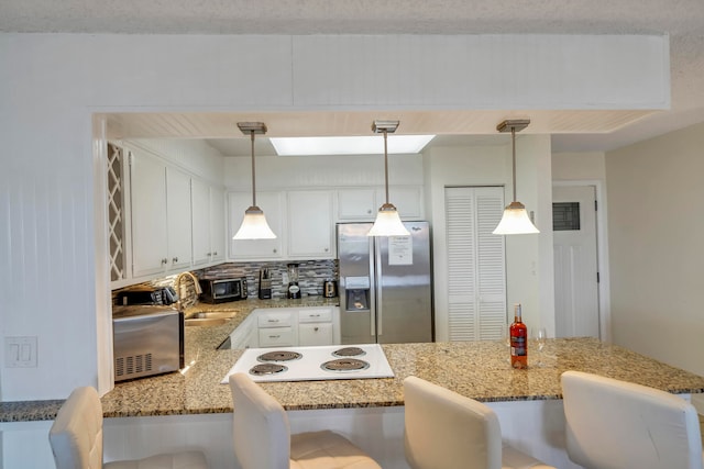 kitchen with appliances with stainless steel finishes, decorative light fixtures, white cabinetry, and a kitchen bar