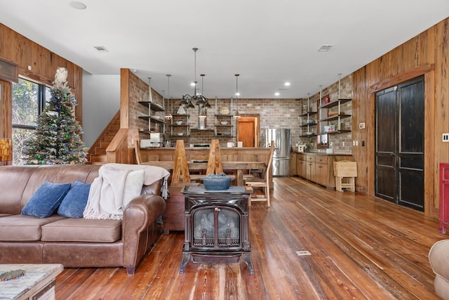 living room with brick wall, wooden walls, a wood stove, and dark hardwood / wood-style floors