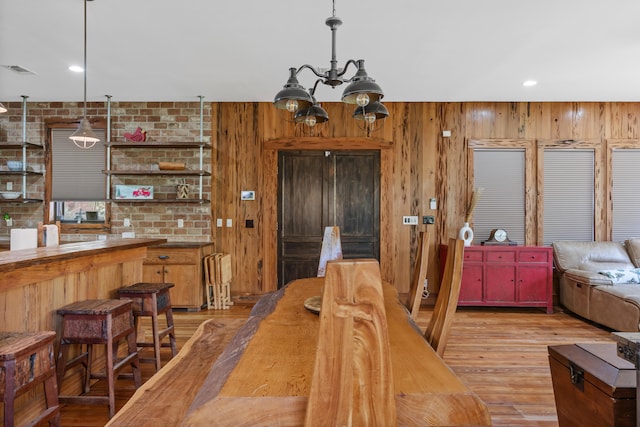 dining room with wood walls, light wood-type flooring, and an inviting chandelier