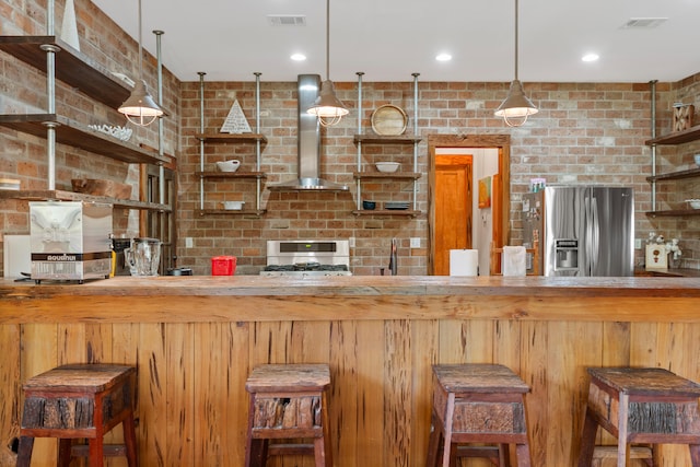 kitchen featuring range hood, brick wall, stainless steel refrigerator with ice dispenser, and a breakfast bar