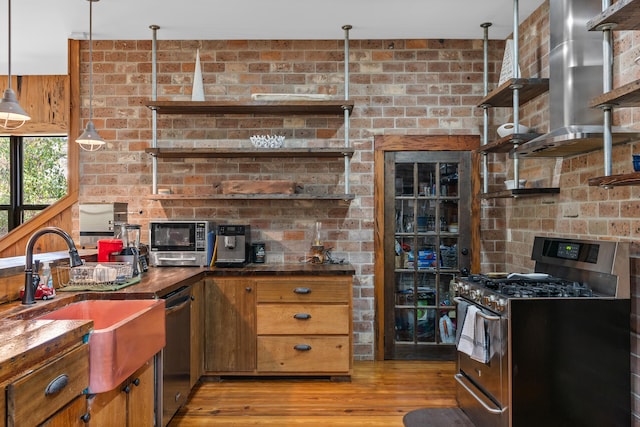 kitchen with stainless steel appliances, pendant lighting, brick wall, and range hood