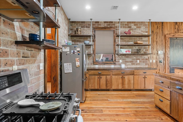 kitchen with brick wall, appliances with stainless steel finishes, light hardwood / wood-style floors, and extractor fan