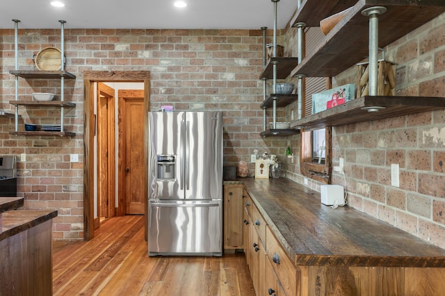 kitchen featuring brick wall, light wood-type flooring, pendant lighting, and stainless steel refrigerator with ice dispenser