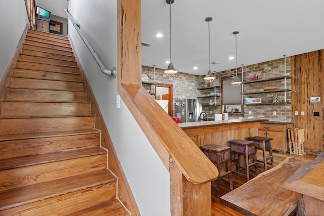 stairs featuring sink, dark wood-type flooring, brick wall, and wooden walls