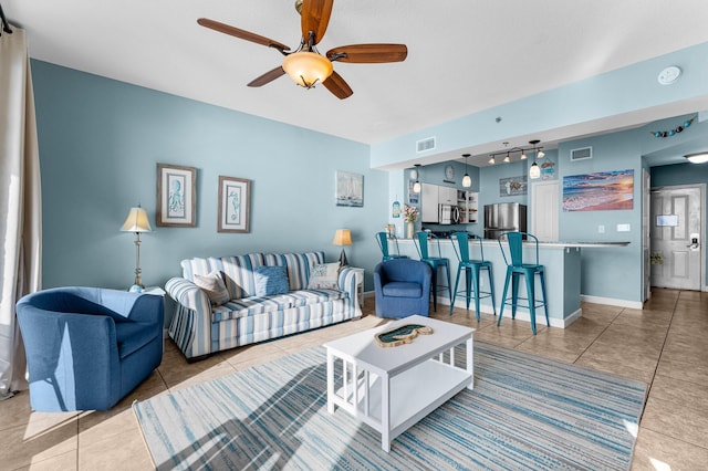 living area featuring tile patterned flooring, visible vents, ceiling fan, and baseboards