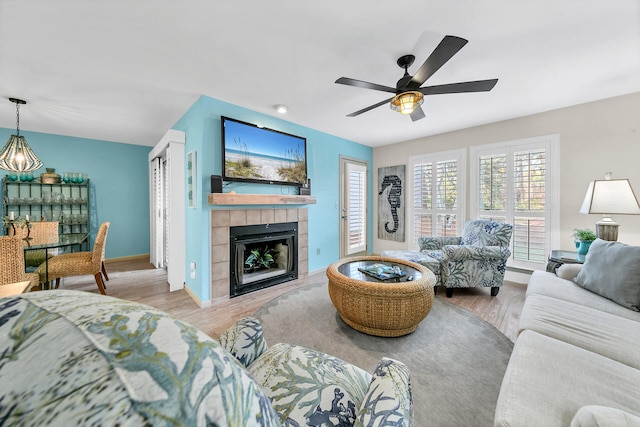 living room with a tiled fireplace, ceiling fan, and light wood-type flooring