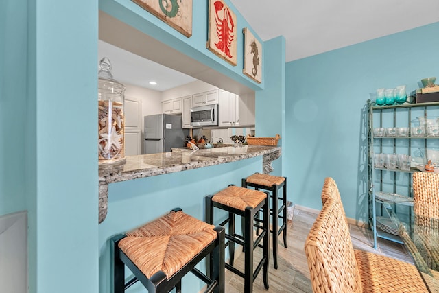 kitchen featuring white cabinets, light stone counters, light hardwood / wood-style flooring, and stainless steel appliances