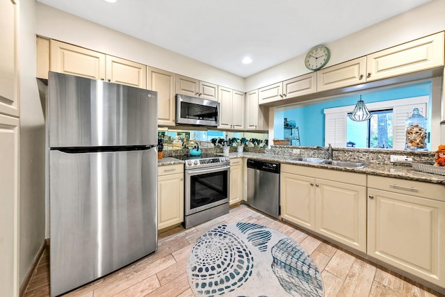 kitchen featuring cream cabinets, stone countertops, stainless steel appliances, light hardwood / wood-style floors, and sink