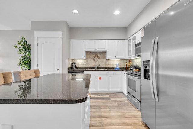 kitchen with white cabinets, light hardwood / wood-style floors, tasteful backsplash, stainless steel appliances, and dark stone countertops