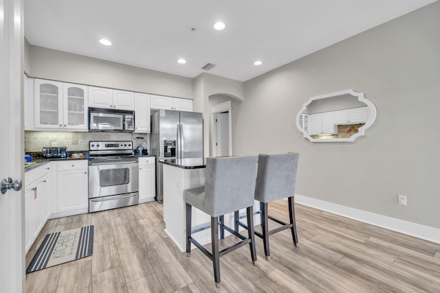 kitchen with a breakfast bar, white cabinets, stainless steel appliances, tasteful backsplash, and light hardwood / wood-style floors