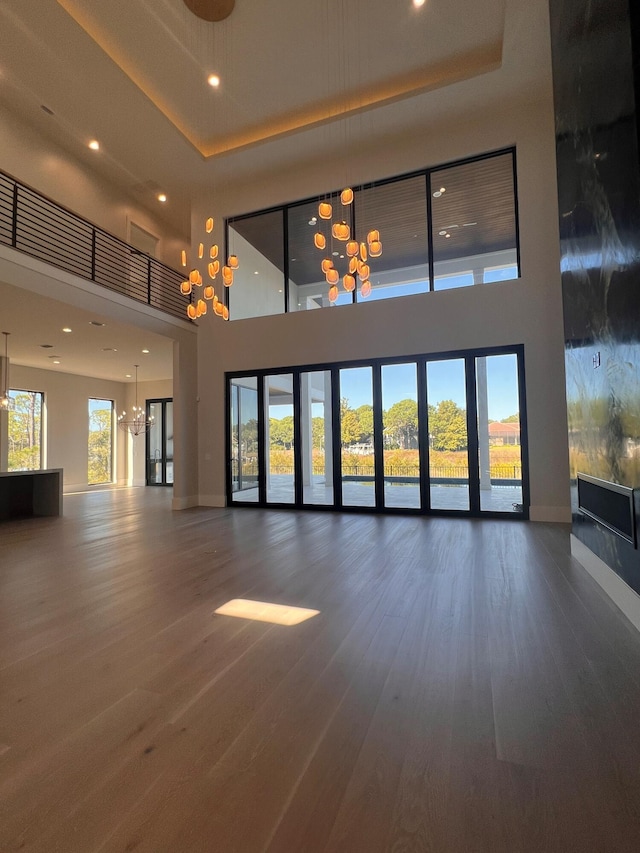 empty room featuring a raised ceiling, dark wood-type flooring, a high ceiling, and an inviting chandelier