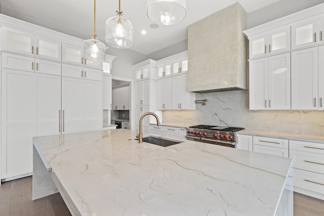 kitchen featuring light stone counters, sink, decorative light fixtures, range with two ovens, and white cabinetry