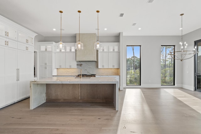 kitchen featuring a large island with sink, white cabinetry, decorative light fixtures, and light wood-type flooring