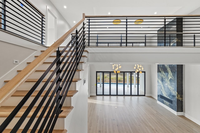 stairway featuring wood-type flooring, a towering ceiling, and an inviting chandelier