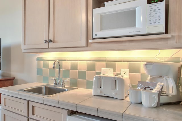 kitchen with backsplash, white microwave, tile counters, and sink