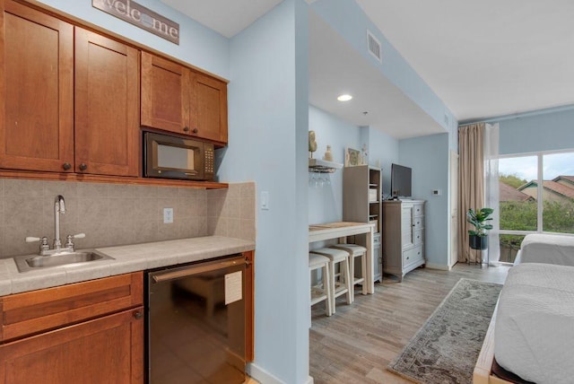 kitchen with black dishwasher, tasteful backsplash, sink, and light wood-type flooring