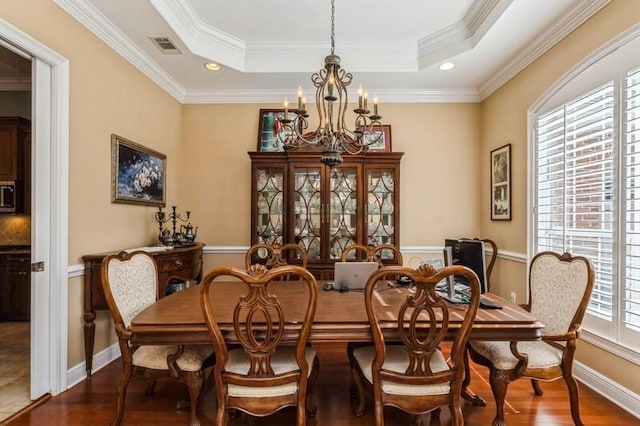 dining area with dark wood-type flooring, a wealth of natural light, a tray ceiling, and an inviting chandelier