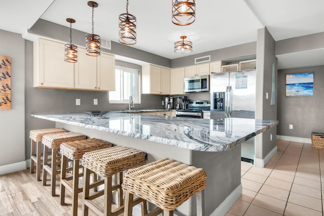 kitchen with decorative light fixtures, light stone counters, appliances with stainless steel finishes, and a breakfast bar area