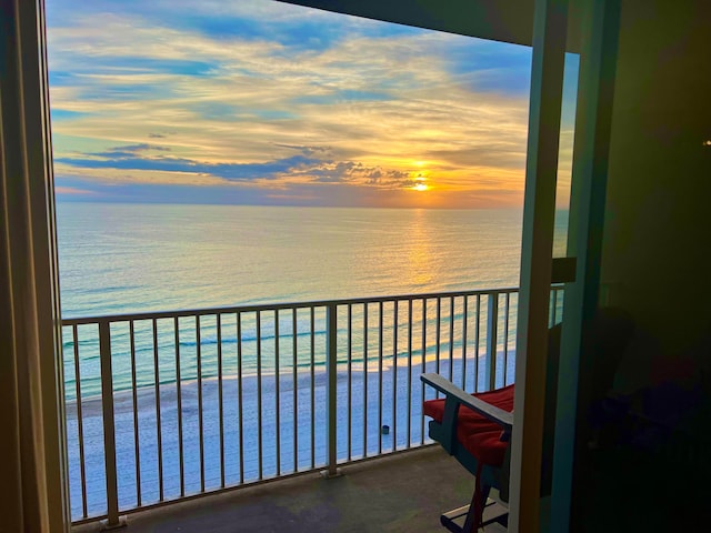 balcony at dusk featuring a beach view and a water view