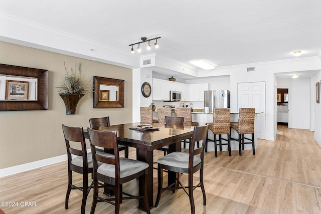 dining space with light wood-type flooring, rail lighting, and ornamental molding