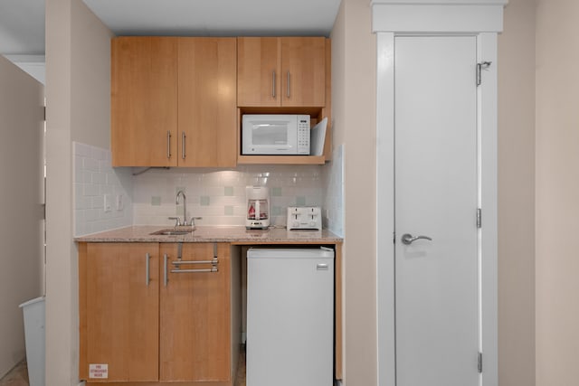 kitchen with light stone countertops, fridge, white microwave, backsplash, and sink