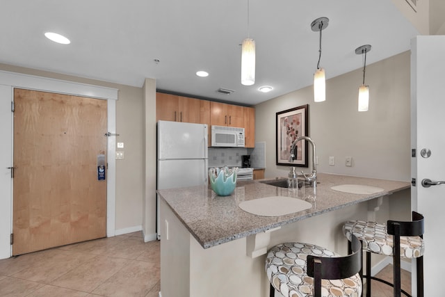 kitchen with white appliances, tasteful backsplash, light stone counters, sink, and pendant lighting