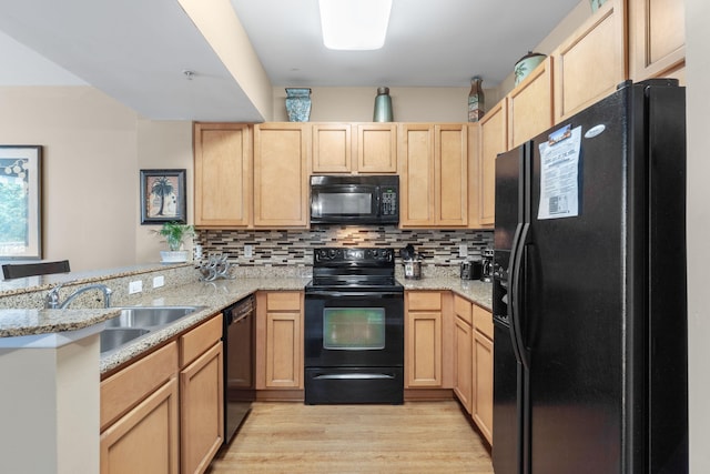 kitchen with kitchen peninsula, light hardwood / wood-style floors, black appliances, light stone counters, and sink