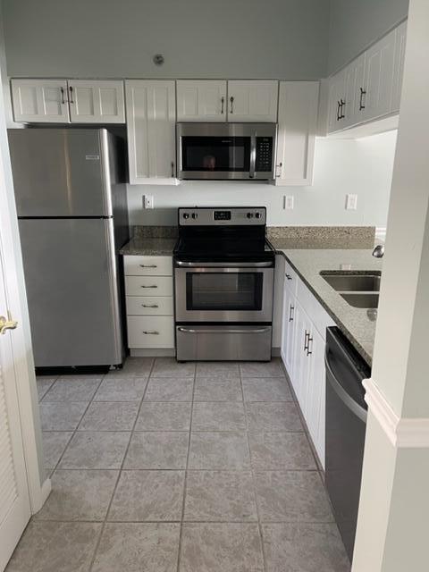 kitchen with dark stone countertops, white cabinetry, stainless steel appliances, and light tile floors