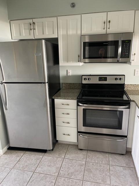 kitchen featuring dark stone counters, stainless steel appliances, white cabinets, and light tile flooring