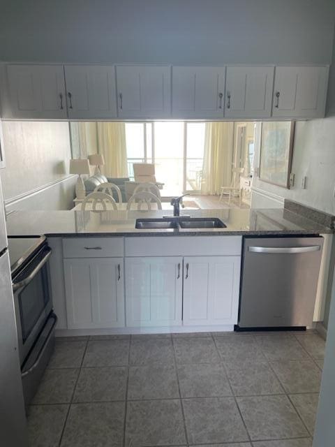 kitchen with electric range oven, white cabinetry, sink, stainless steel dishwasher, and dark stone countertops