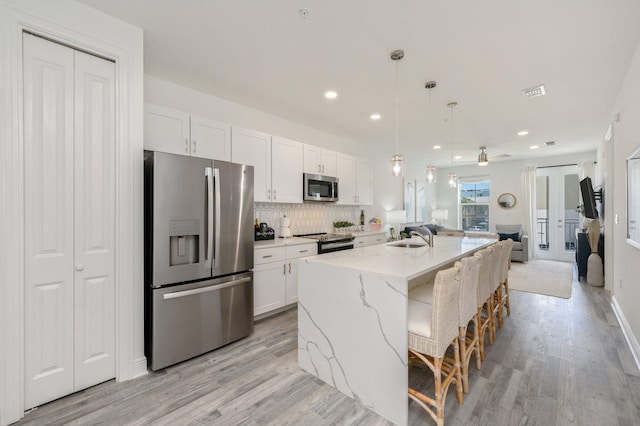 kitchen featuring appliances with stainless steel finishes, a kitchen island with sink, white cabinetry, light hardwood / wood-style flooring, and pendant lighting