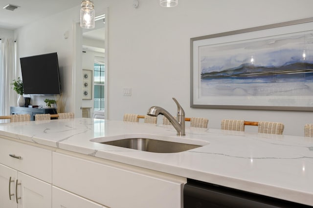 kitchen featuring hanging light fixtures, dishwashing machine, light stone countertops, white cabinetry, and sink