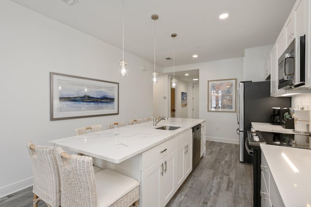 kitchen featuring appliances with stainless steel finishes, light hardwood / wood-style flooring, hanging light fixtures, a center island with sink, and white cabinetry