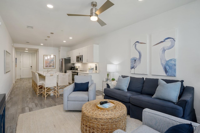 living room featuring ceiling fan, sink, and light wood-type flooring