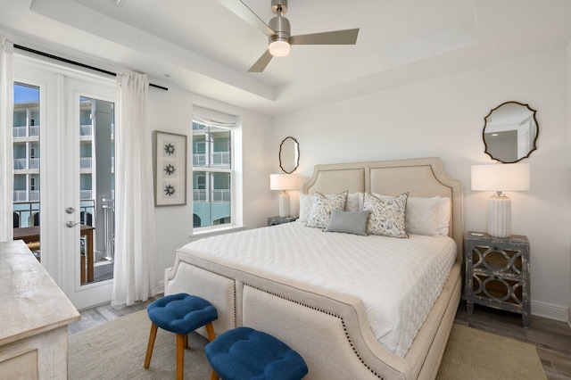 bedroom featuring light hardwood / wood-style flooring, a raised ceiling, ceiling fan, and access to outside